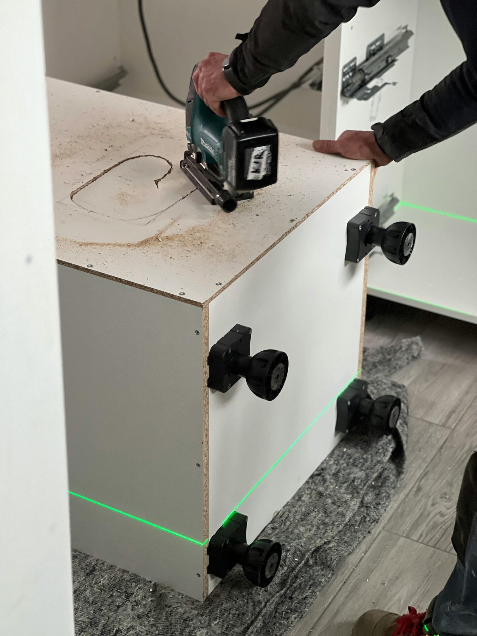 Close-up of a man skillfully using a jigsaw to cut a white kitchen cabinet, showcasing precision carpentry work.