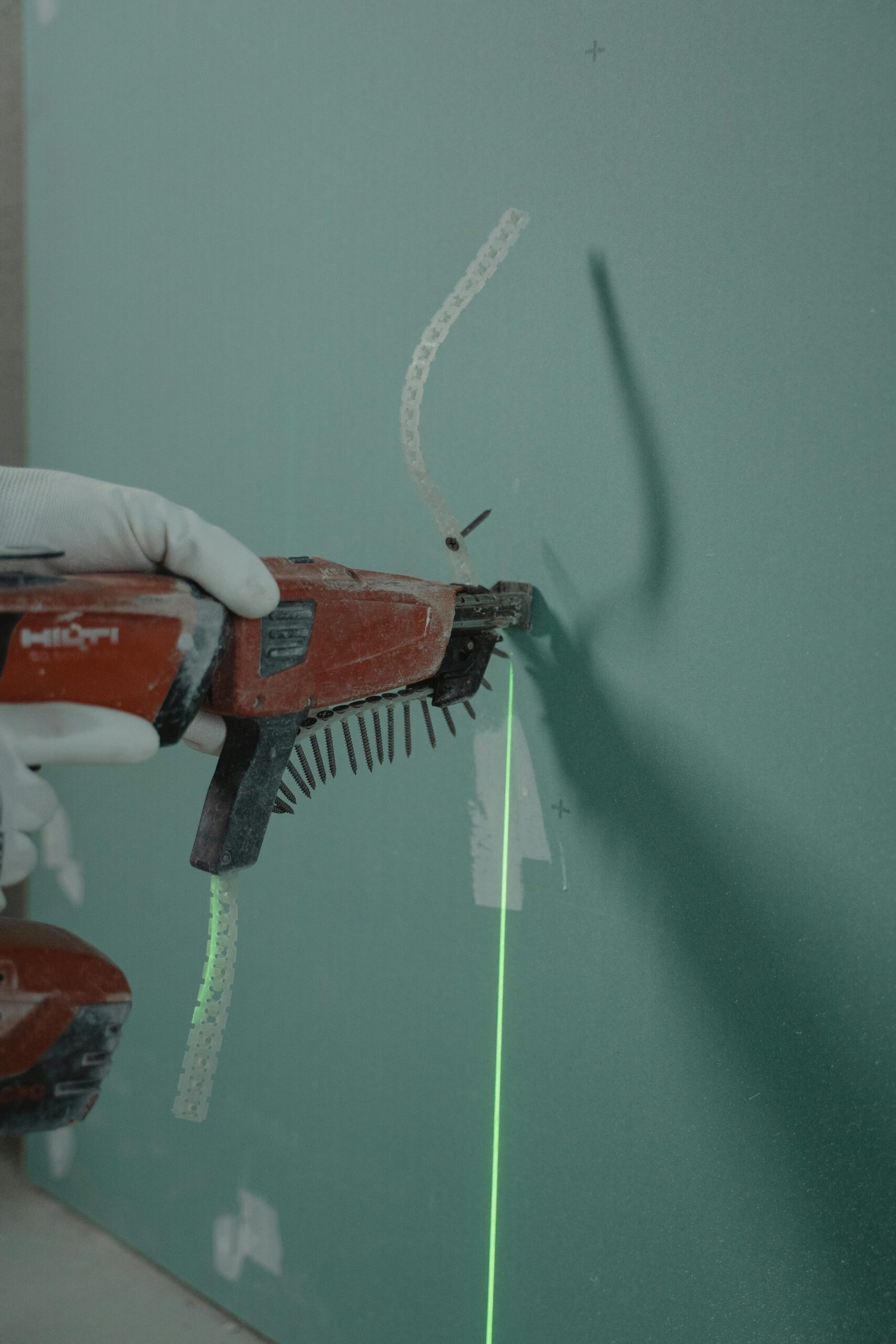 Close-up of a handyman using a laser level and nail gun for drywall installation.